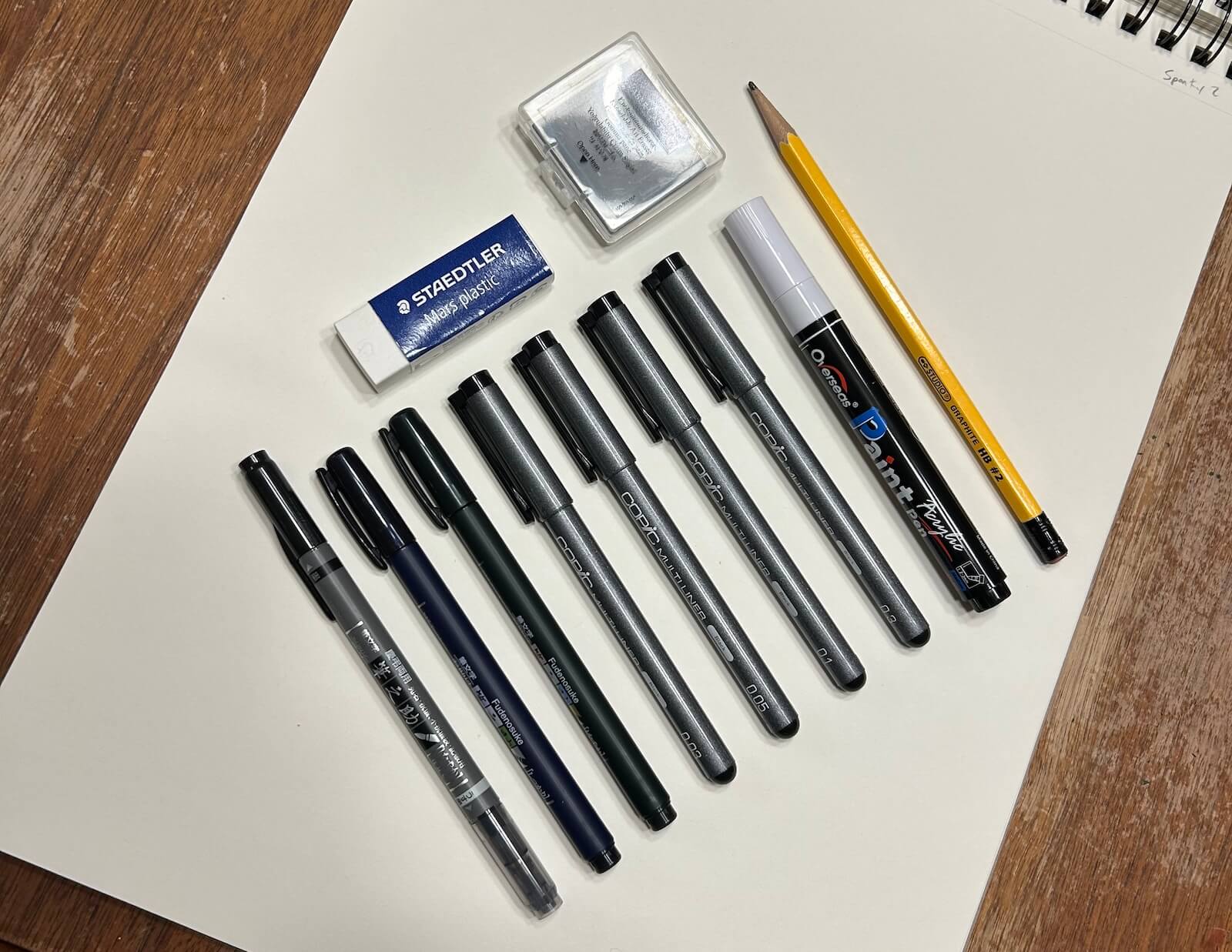 A bunch of drawing pens lined up with a couple erasers and a pencil